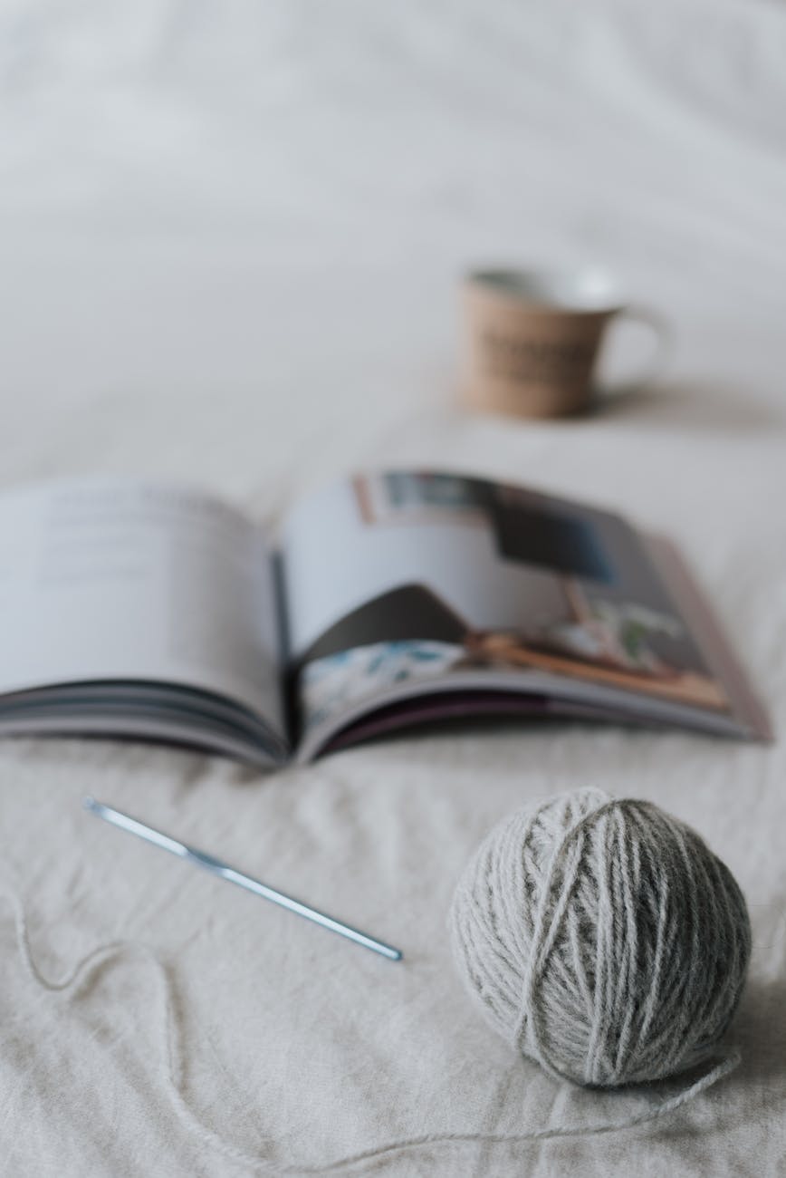 yarn ball and needle placed on bed near opened magazine